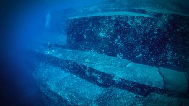 Plongeur explorant l'immense structure rocheuse en forme de pyramide à degrés du monument de Yonaguni au Japon.